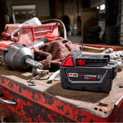 Milwaukee red lithium battery on a toolbox with other tools in a work shop setting.